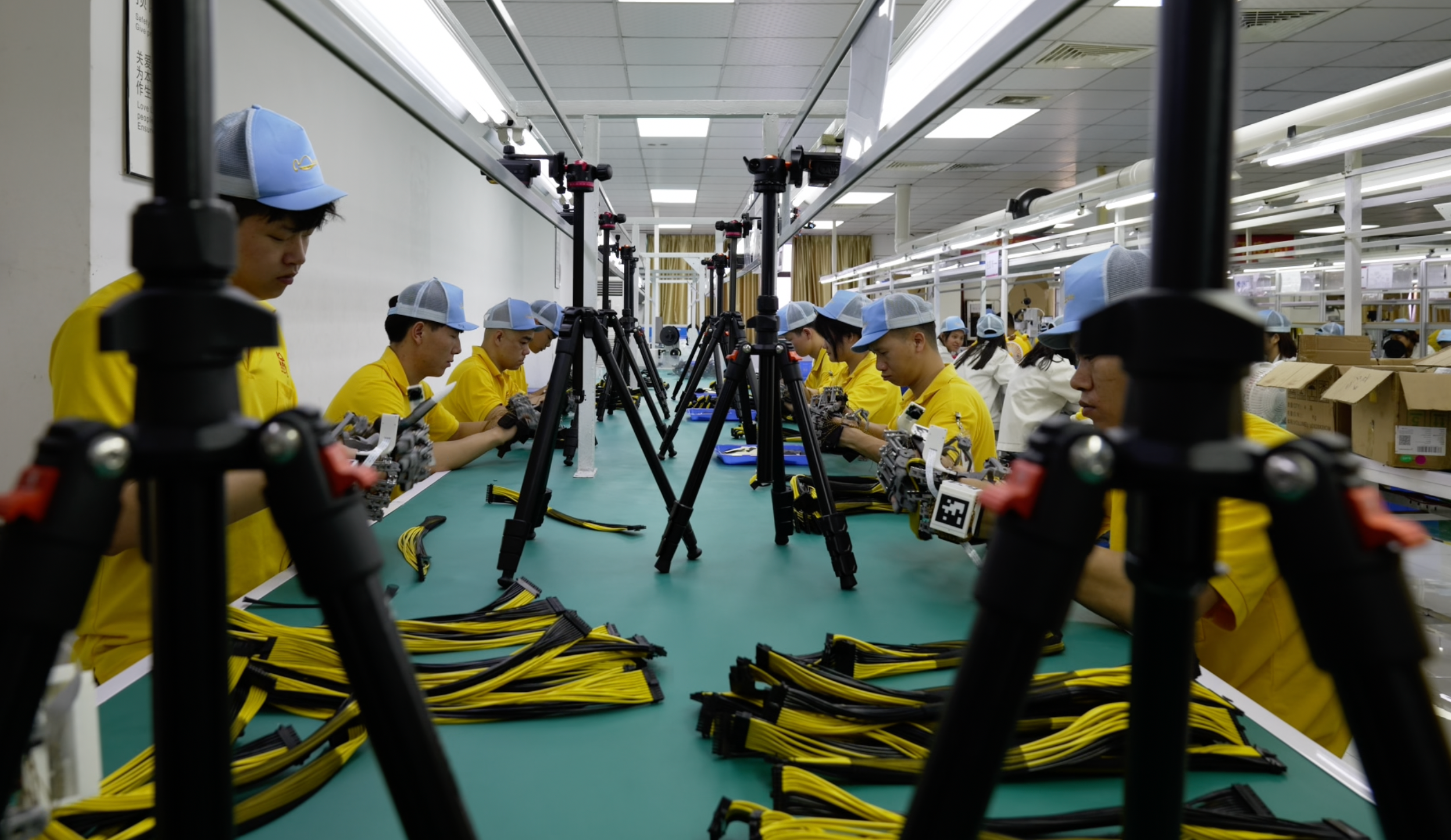 Workers wearing the earlier glove at a factory workbench, with cameras positioned along the table.
