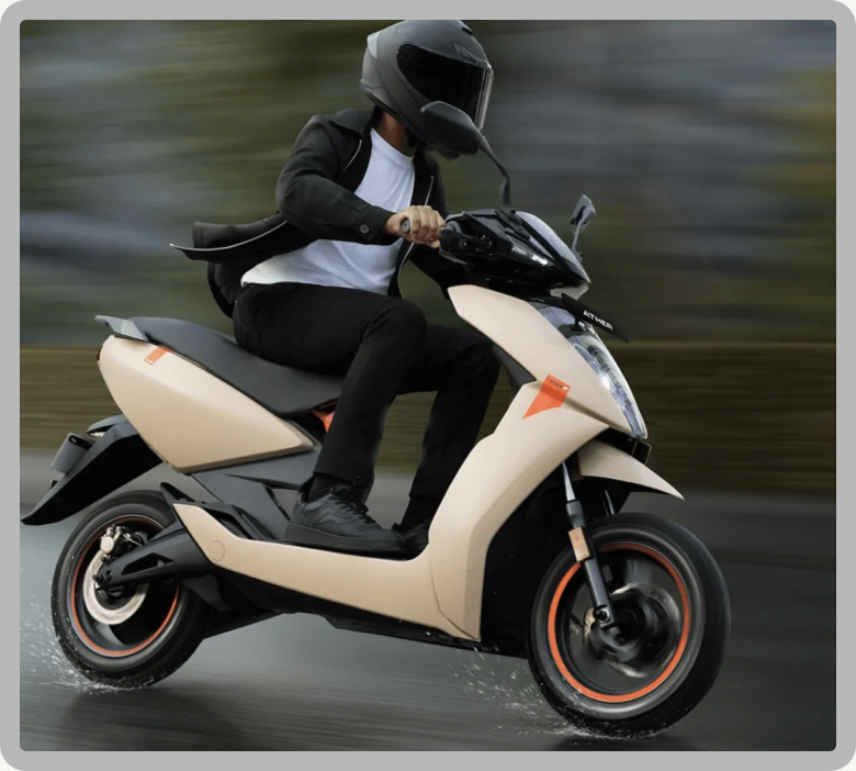 A rider in a black helmet and jacket on a cream Ather 450 scooter, speeding through a blurred green and grey background
