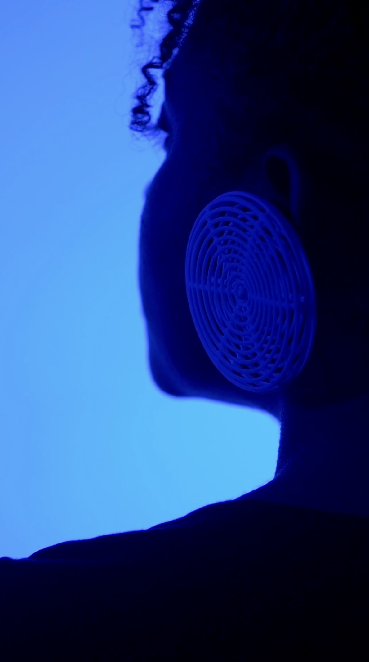 Portrait of a woman wearing a ceramic earring from the Ceramica Collection, shot in monochrome blue light.