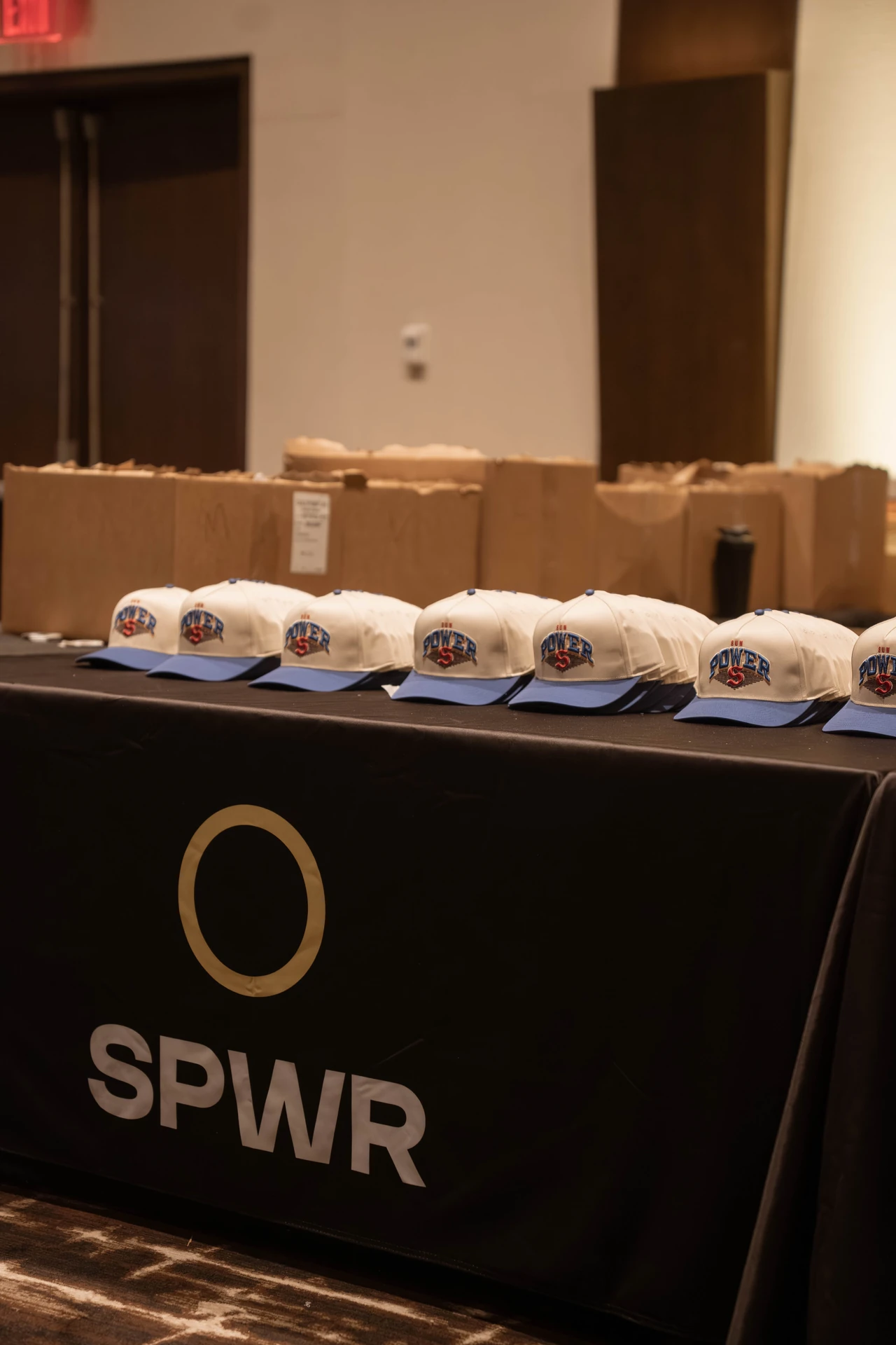 Event hats arranged on a black tablecloth with a yellow ring and white SPWR wordmark.
