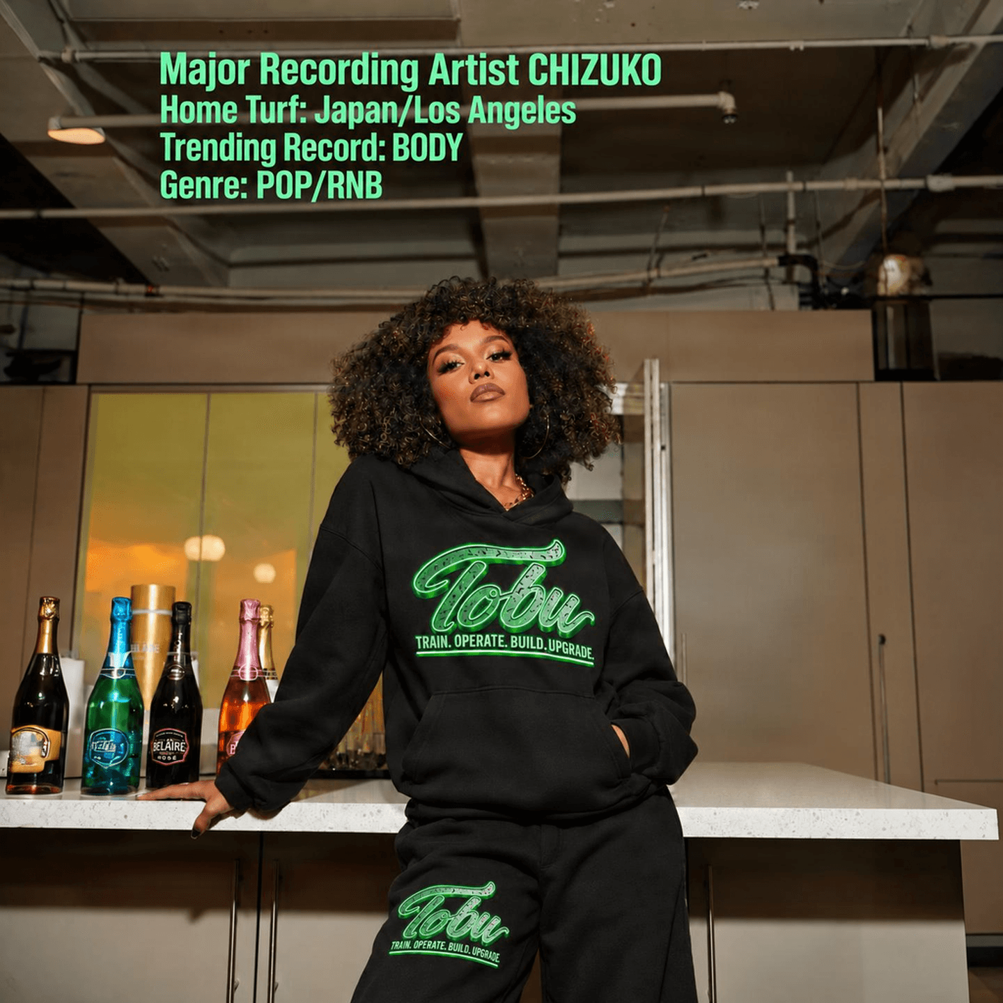 CHIZUKO wearing a black TOBU hoodie and sweatpants with green Train. Operate. Build. Upgrade. branding