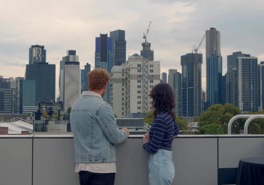 Two people standing on a balcony, looking at a city skyline.