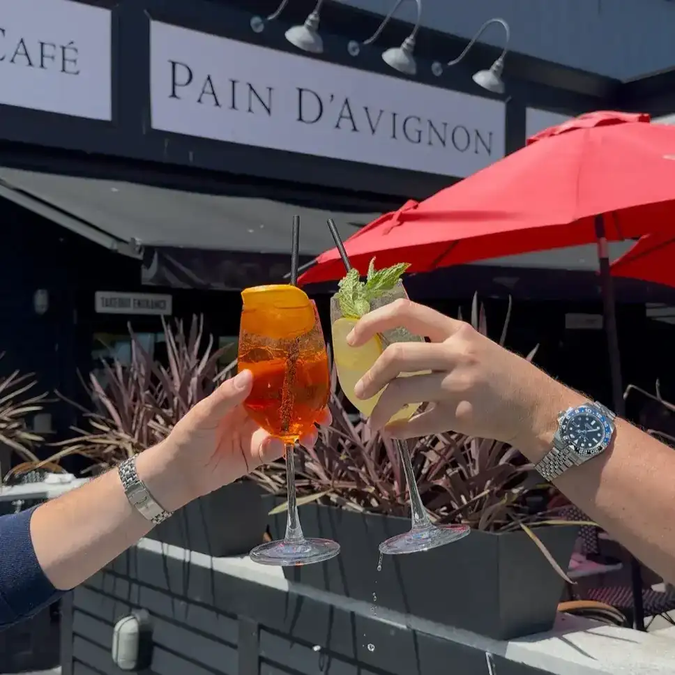 Two guests toasting colorful cocktails outside Pain D’Avignon restaurant patio in Hyannis.