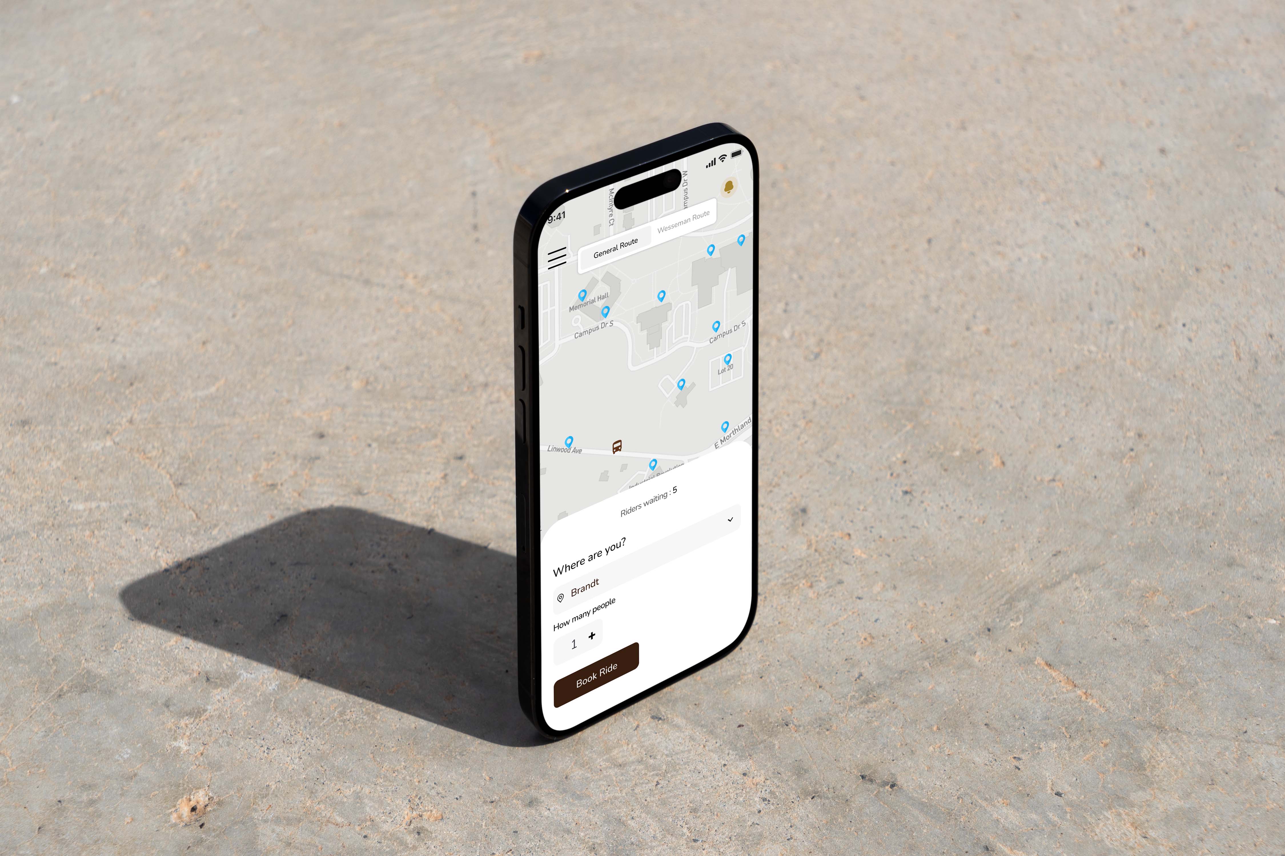A black smartphone displaying a map application with multiple location pins is set upright on a textured, light gray concrete surface, casting a shadow to the side.