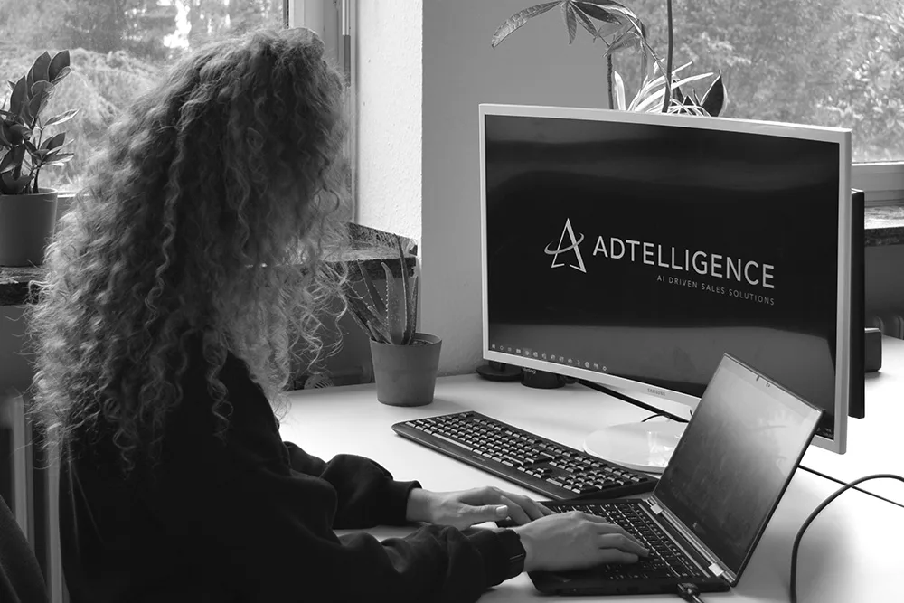Mitarbeiterin am Arbeitsplatz mit ADTELLIGENCE-Logo auf dem Bildschirm