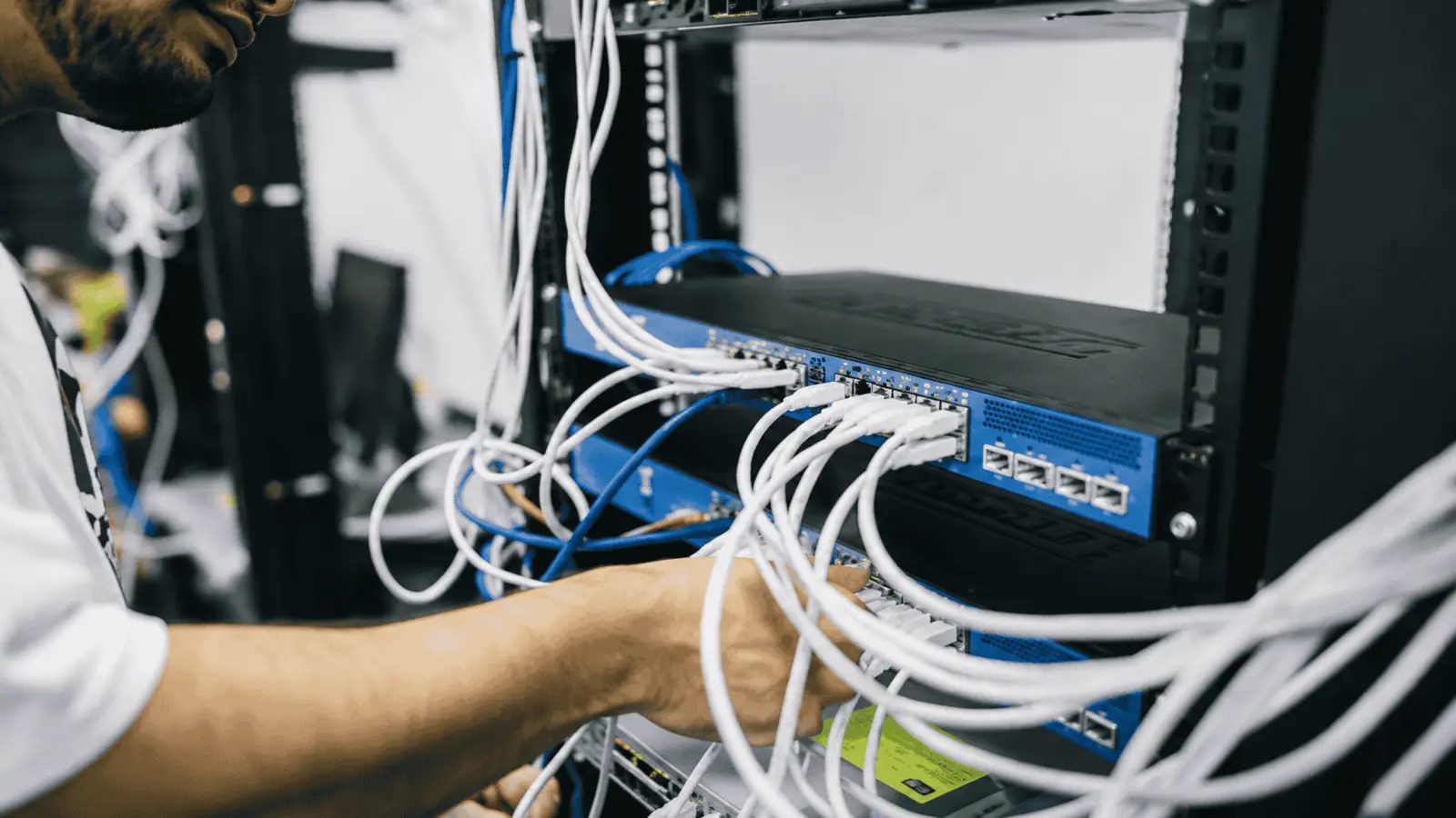 Technician plugging Ethernet patch cables into rack-mounted network switches