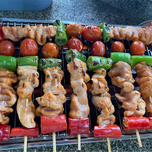 Grilled skewers with chicken, cherry tomatoes, green peppers, and red bell peppers on a metal grate.