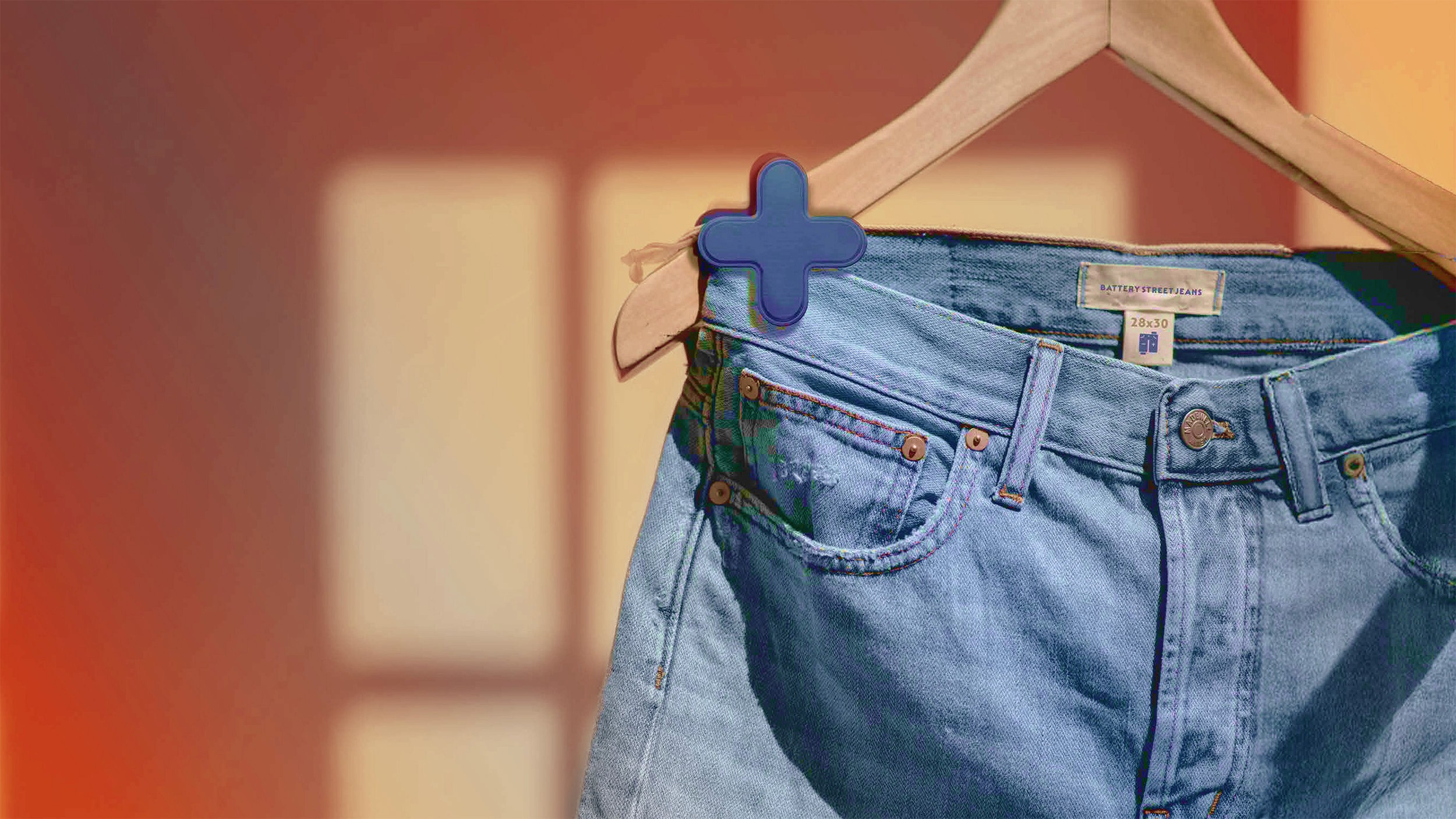A pair of light blue denim jeans hangs from a wooden hanger against a blurred warm-toned background featuring shadows and soft lighting.