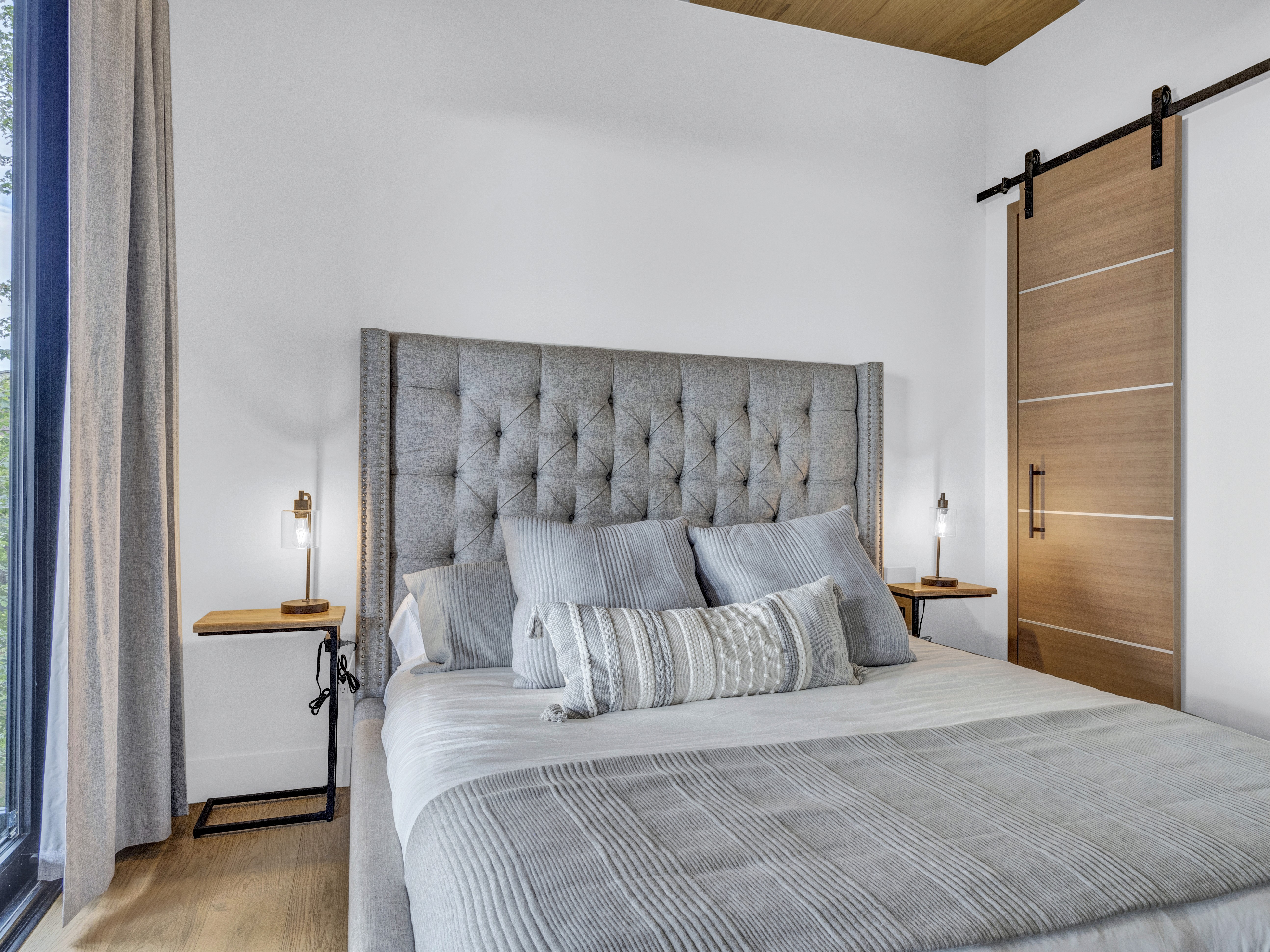 Modern guest room with a tall grey headboard and a stylish light-wood sliding barn door