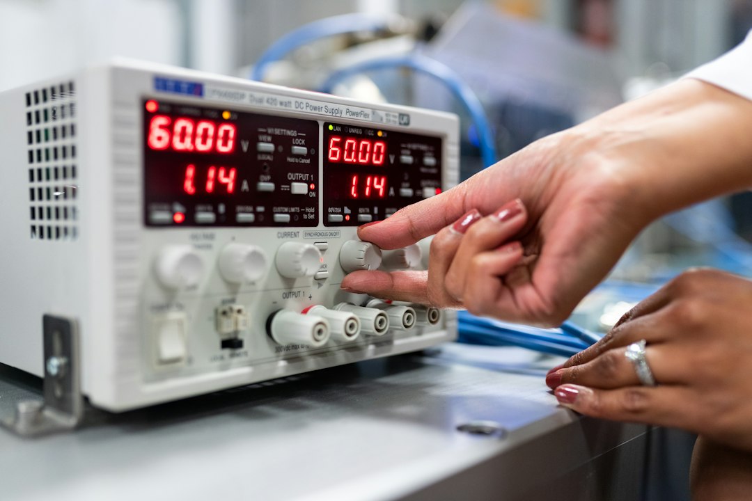 a technician’s hand using a specialized diagnostic tool with a small screen connected to a large silver HVAC outdoor unit, tools spread neatly on a canvas mat on the grass nearby, sunlight reflecting off the metal machinery
