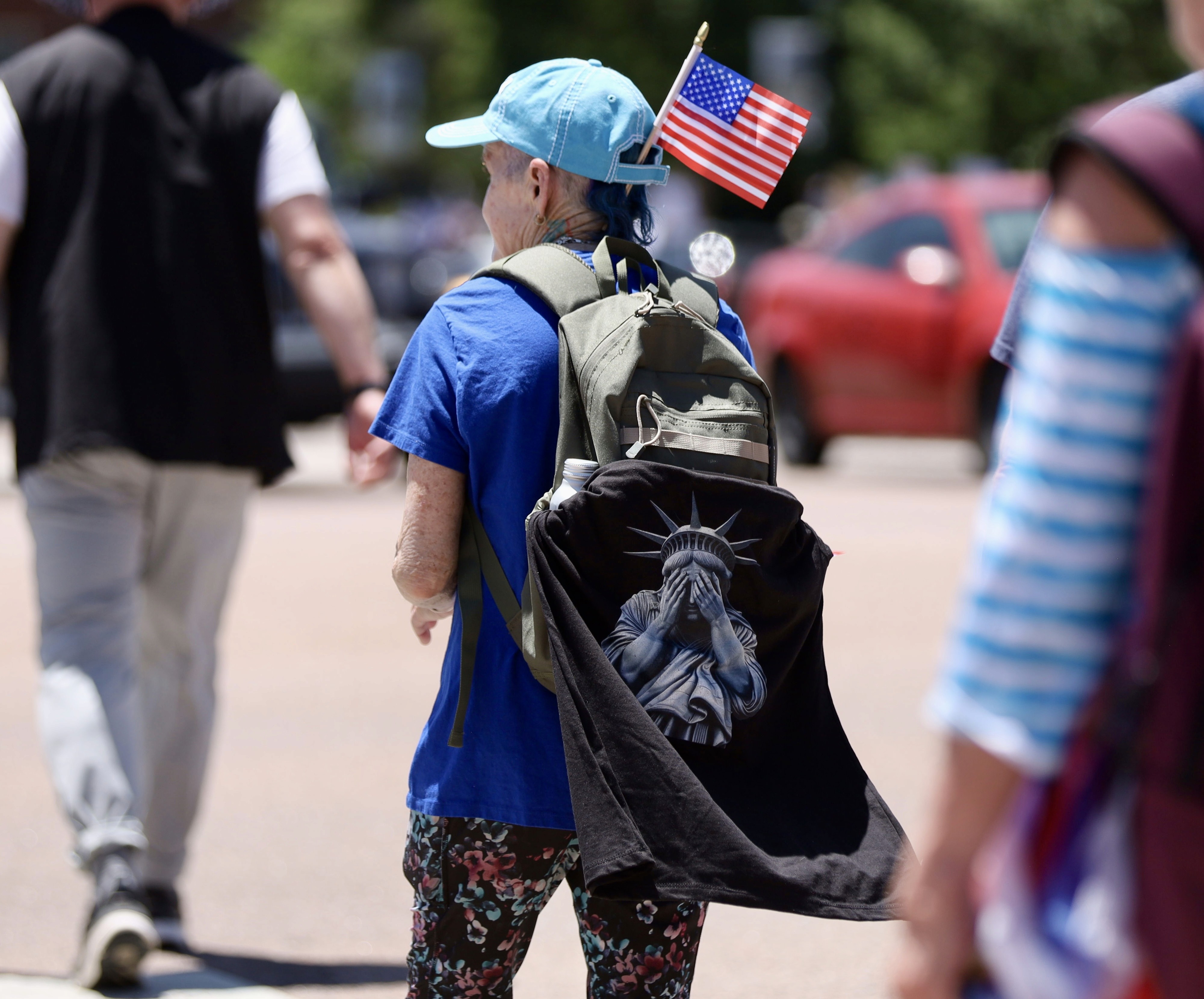 Credit: Trish Kantor. A protester with a backpack and American flag stands in front of a crowd.