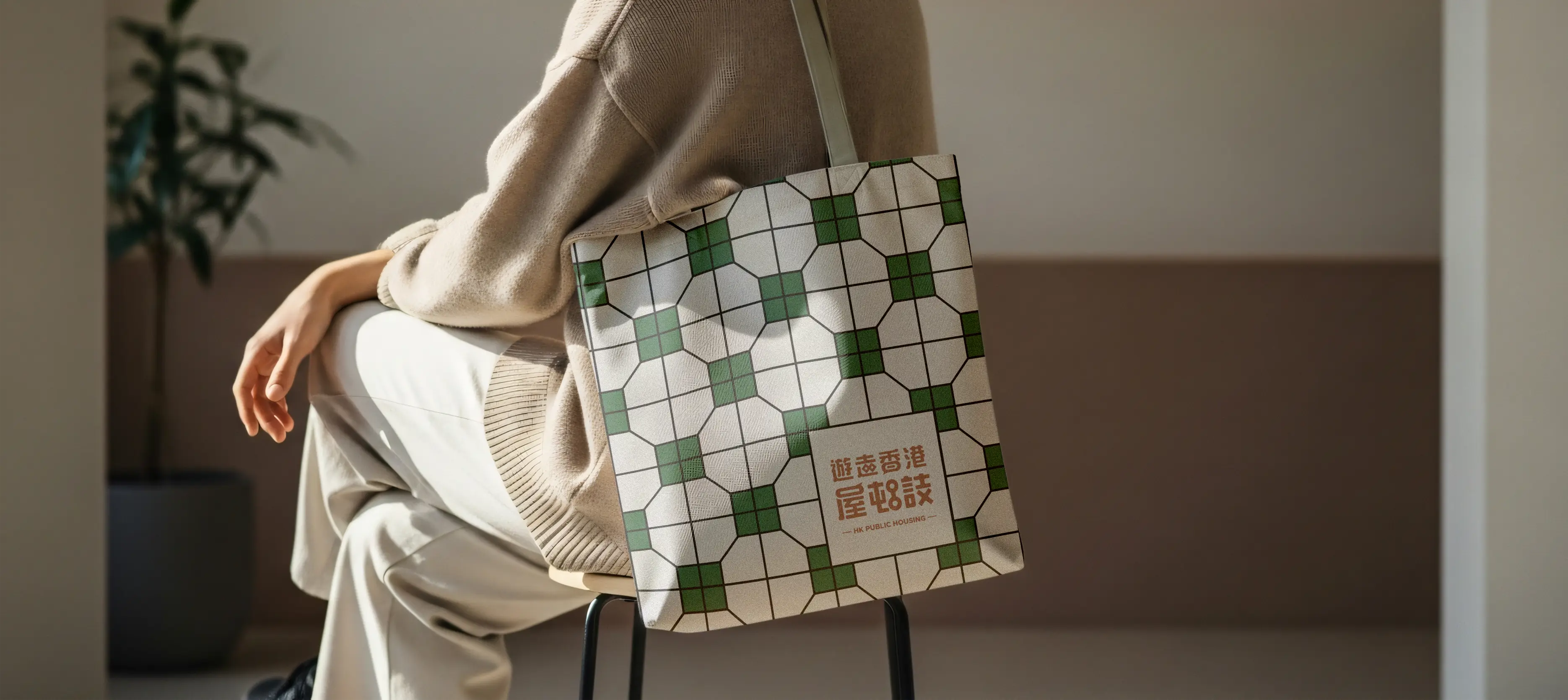 HK Public Housing visual identity application – canvas tote bag with green-white geometric grid pattern and Chinese typography “遊走香港屋邨” on chair, evoking community heritage and everyday belonging by Teatime Studio.