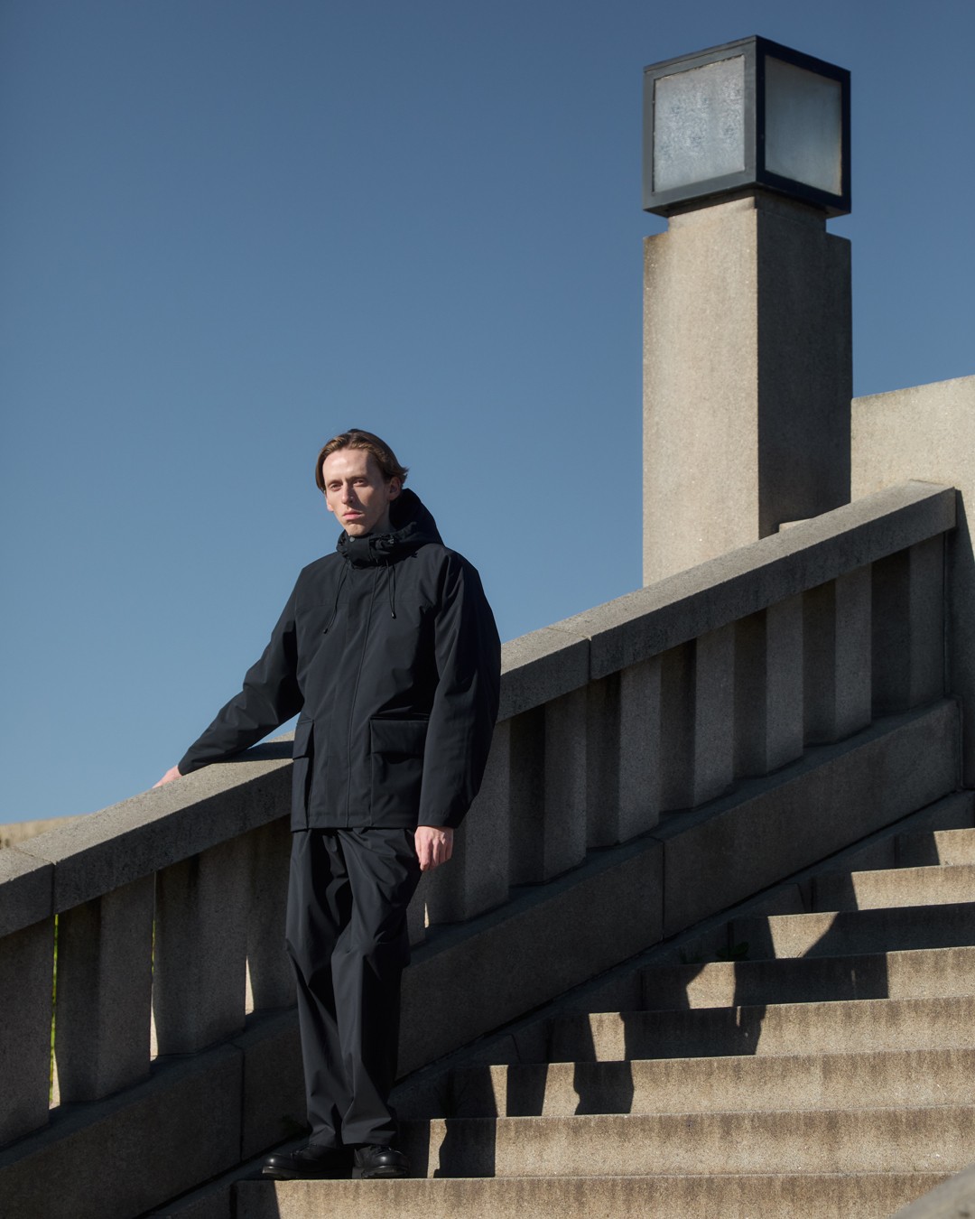 Homme posant sur des escaliers portant une parka technique noire dans le lookbook de Norse Projects