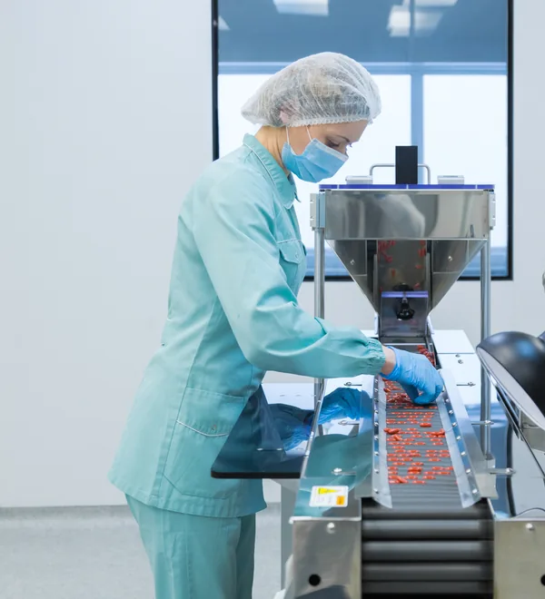 Cleanroom operator in gown, hairnet and mask inspecting tablets on a production line