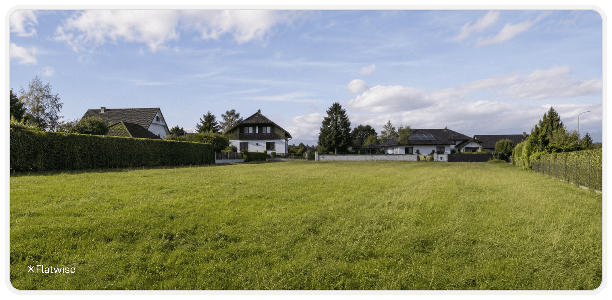 Großes unbebautes Grundstück in einer ruhigen Wohnsiedlung mit grüner Wiese, Einfamilienhäusern im Hintergrund und blauem Himmel. Das Bild zeigt eine typische Parzelle für mögliche Bebauung oder Parzellierung.