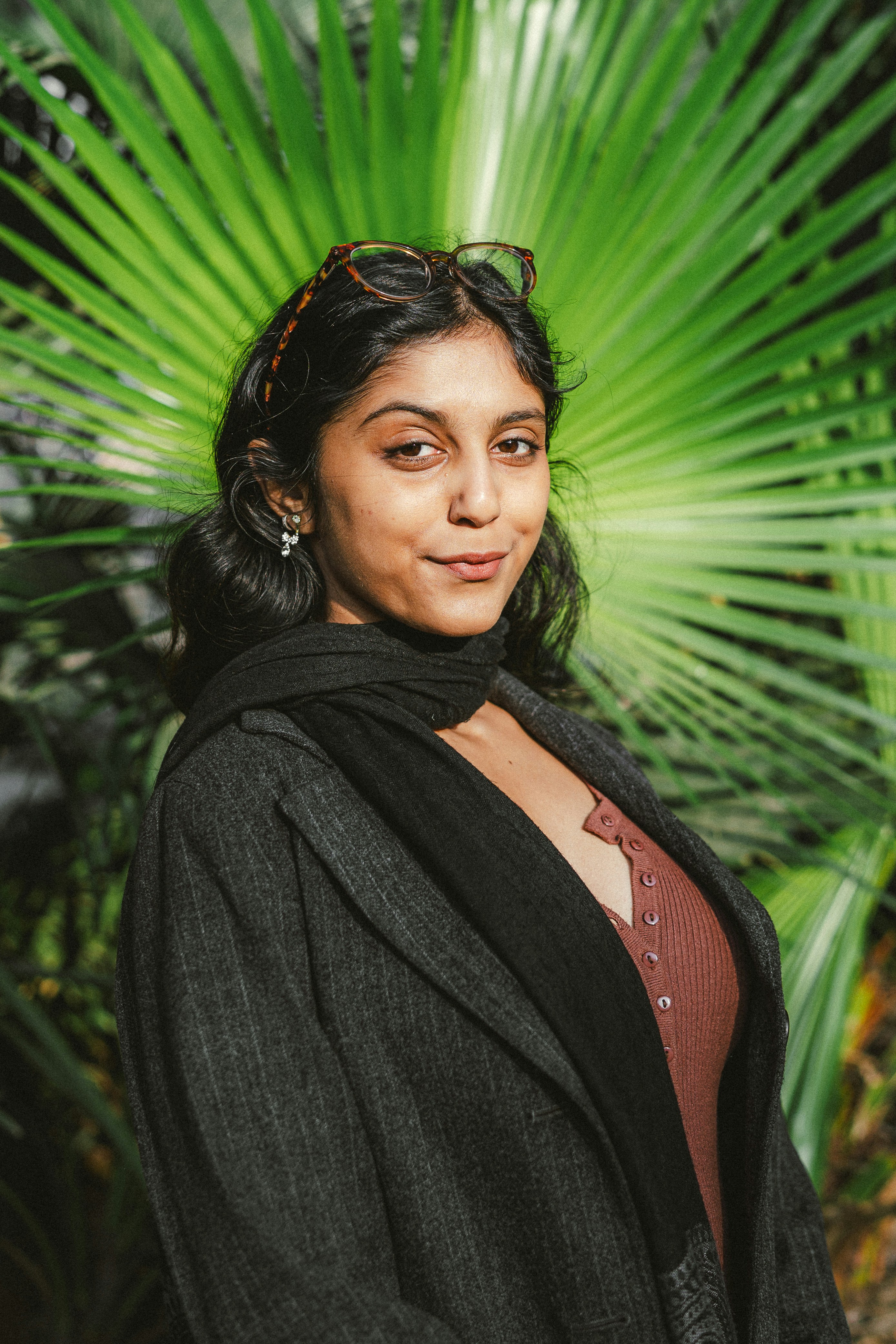Woman in coat stands before a large green palm leaf.