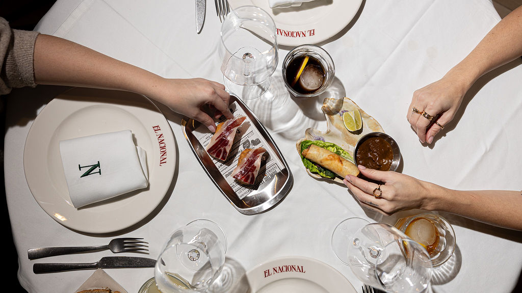 White plate with roasted chicken served in a golden sauce with herbs and capers, placed on a terrazzo tabletop in sunlight.