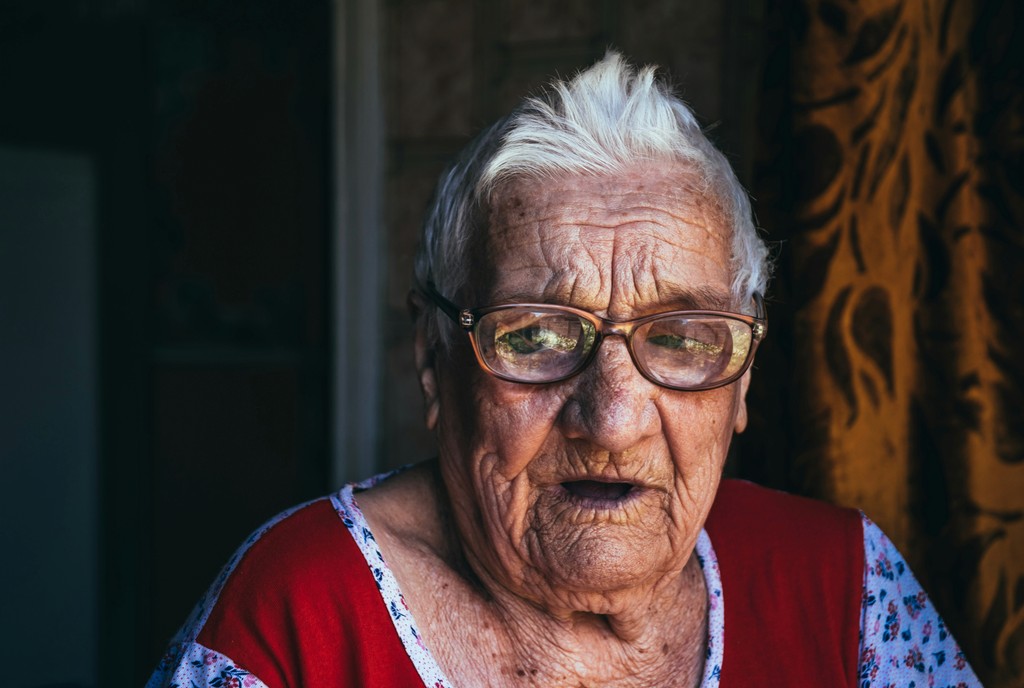 A close-up portrait of an elderly woman with white hair and glasses, wearing a red and floral dress, capturing the essence of aging and wisdom.