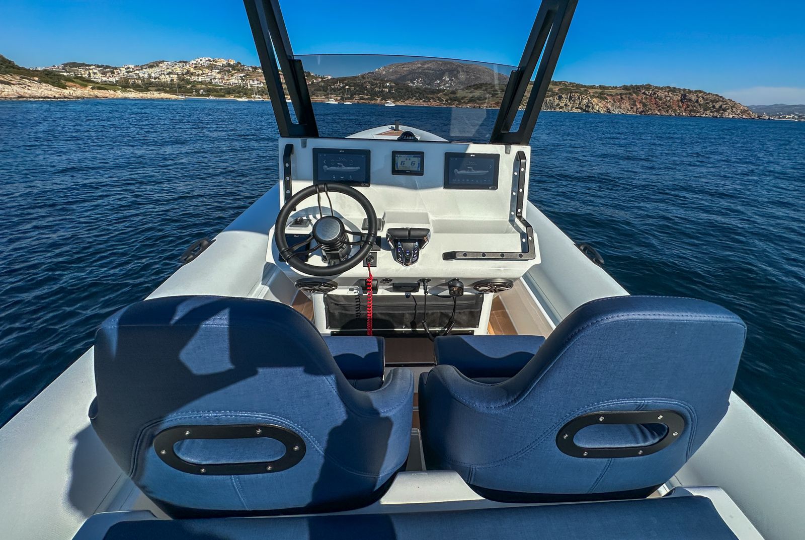 White Rock 36 speedboat with captain at helm cruising calm blue waters near Paros coastline with hills in background.