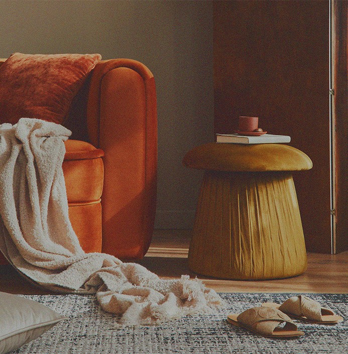 Throw blanket tossed along cozy orange velvet chair, in room next to journal and cup.
