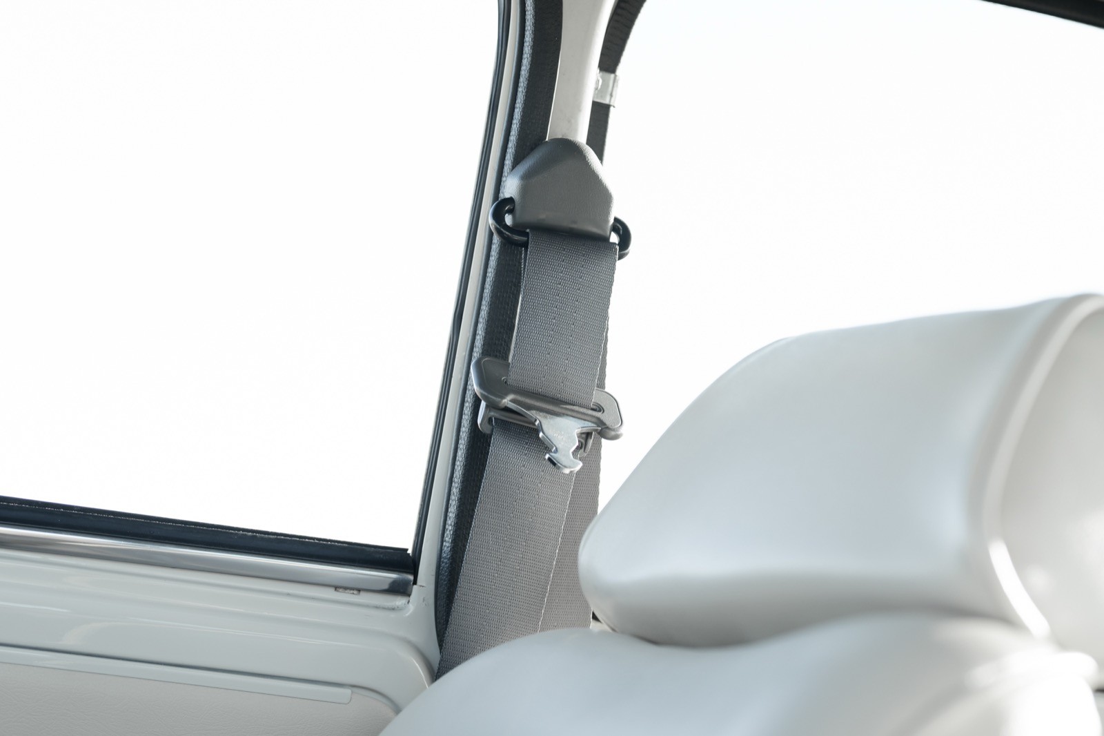 Close-up of a car's interior showing a headrest and part of the window frame against a bright background.