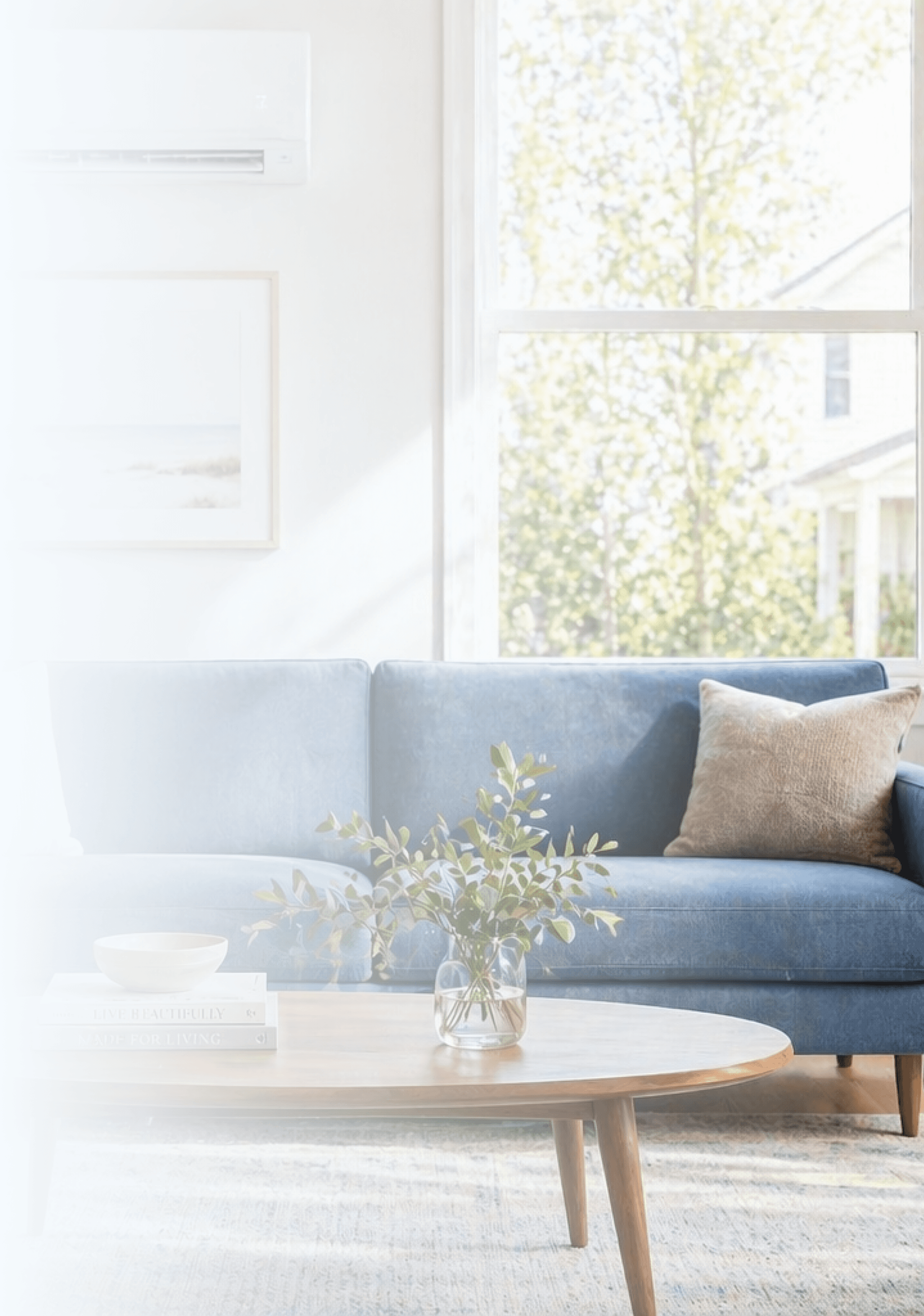 Bright modern living room with a blue sofa, wooden coffee table, plants, built-in shelves, and a large sunlit window.