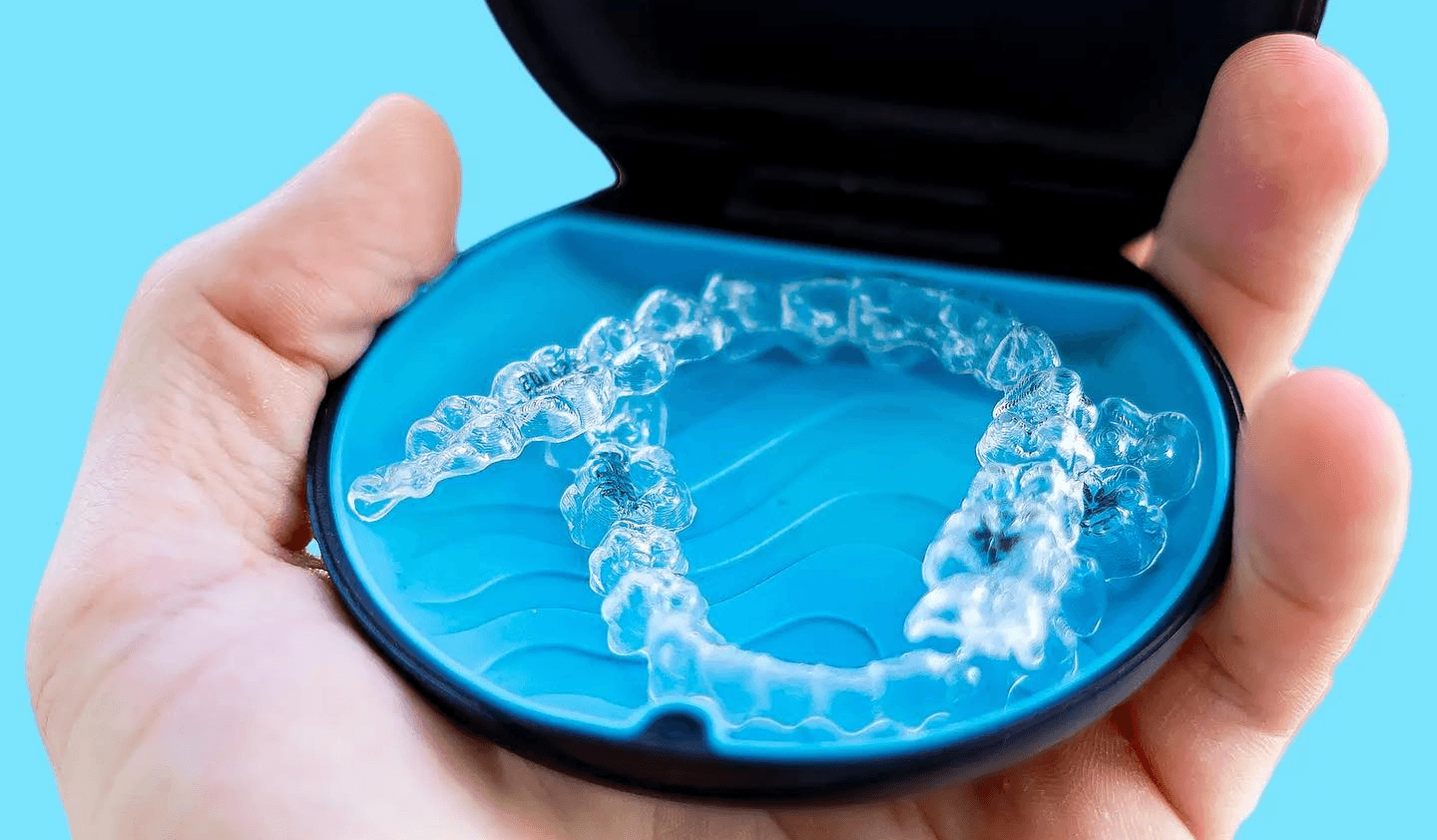 Hand holding Invisalign® clear aligners for gap teeth treatment. 