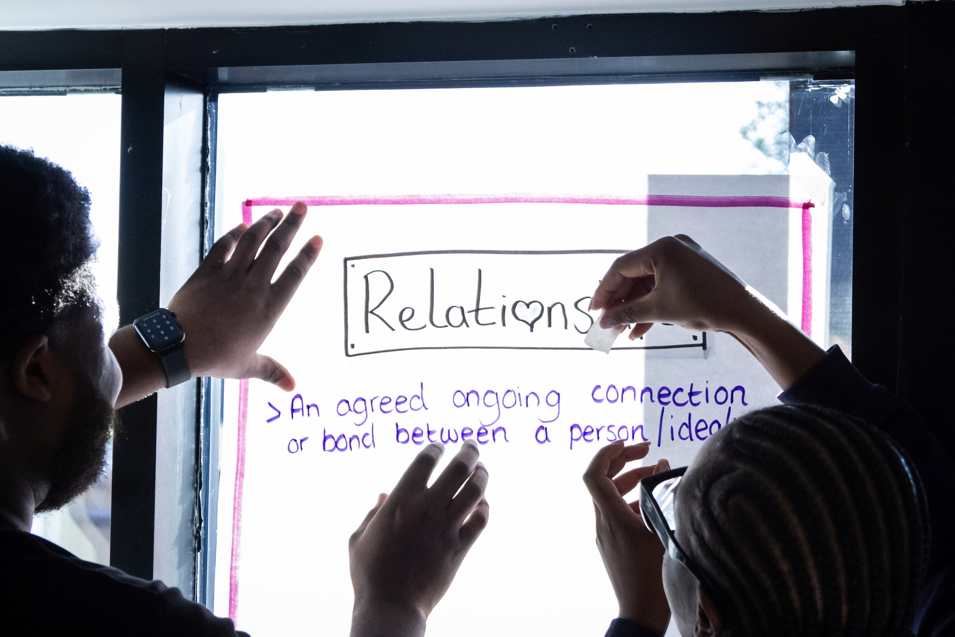 Two people sticking a flip chart on the window. 
