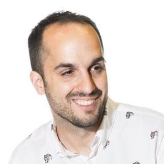 A smiling person with short hair, wearing a patterned shirt against a light background.