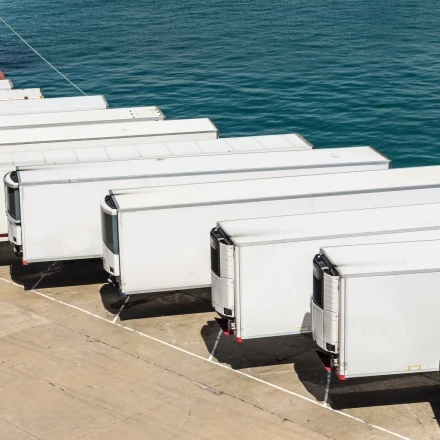 White refrigerated semi-trailers lined up at a waterfront loading dock