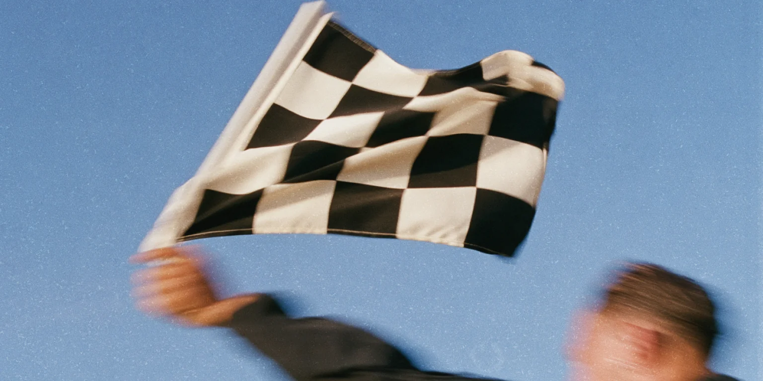 Person waving a chequered racing flag against a blue sky.