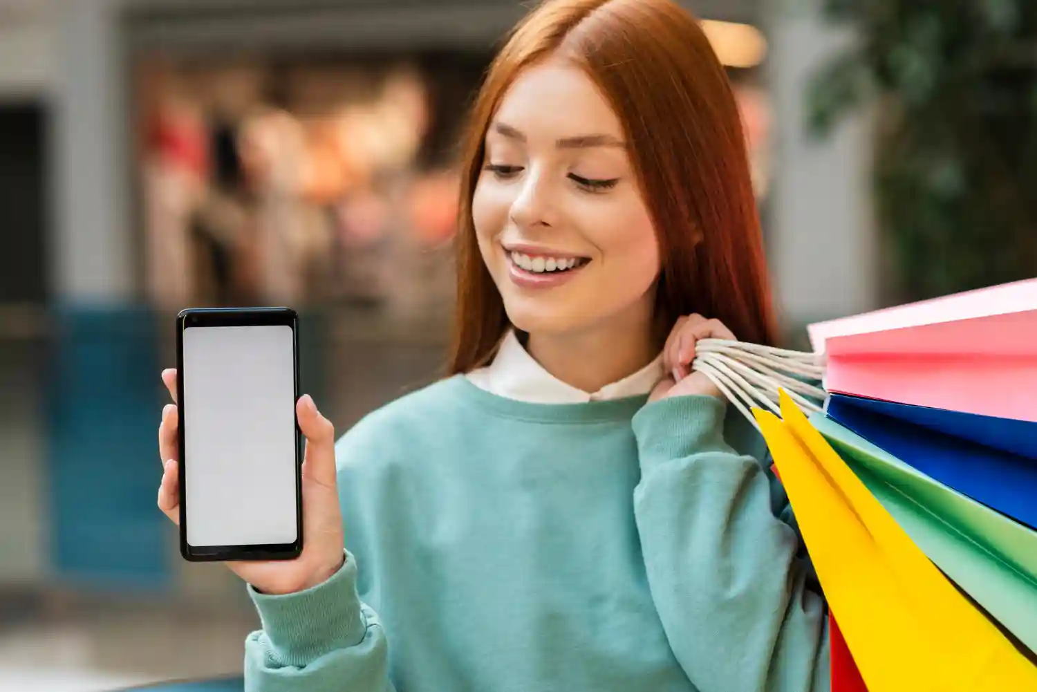 A smiling woman holding shopping bags shows a blank smartphone screen for a mobile shopping blog post.