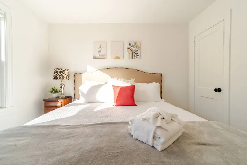 King bed with a tan headboard, a red accent pillow and folded towels