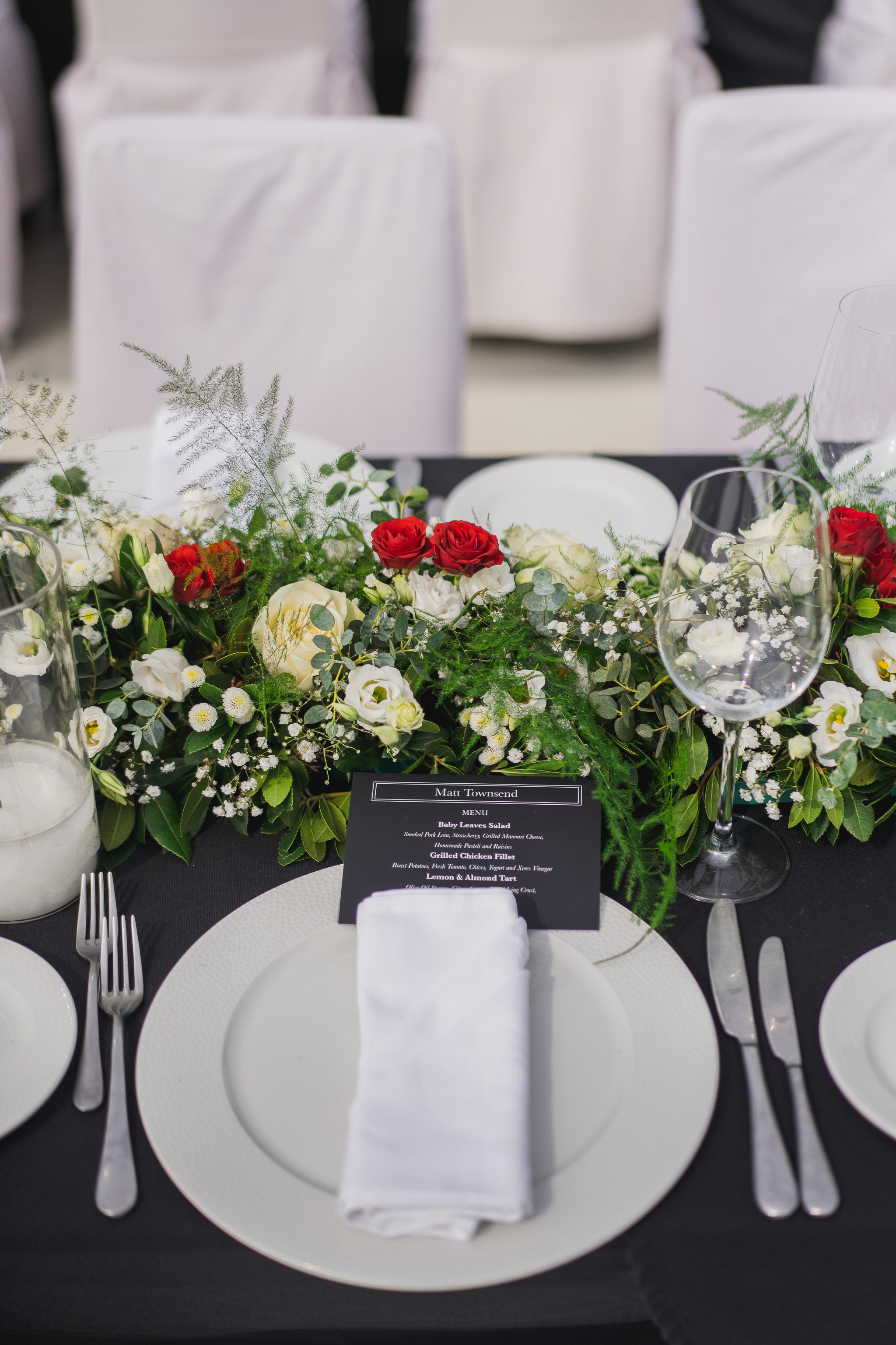 Close-up detail of an elegant white floral centerpiece and place setting on a rustic wooden wedding table