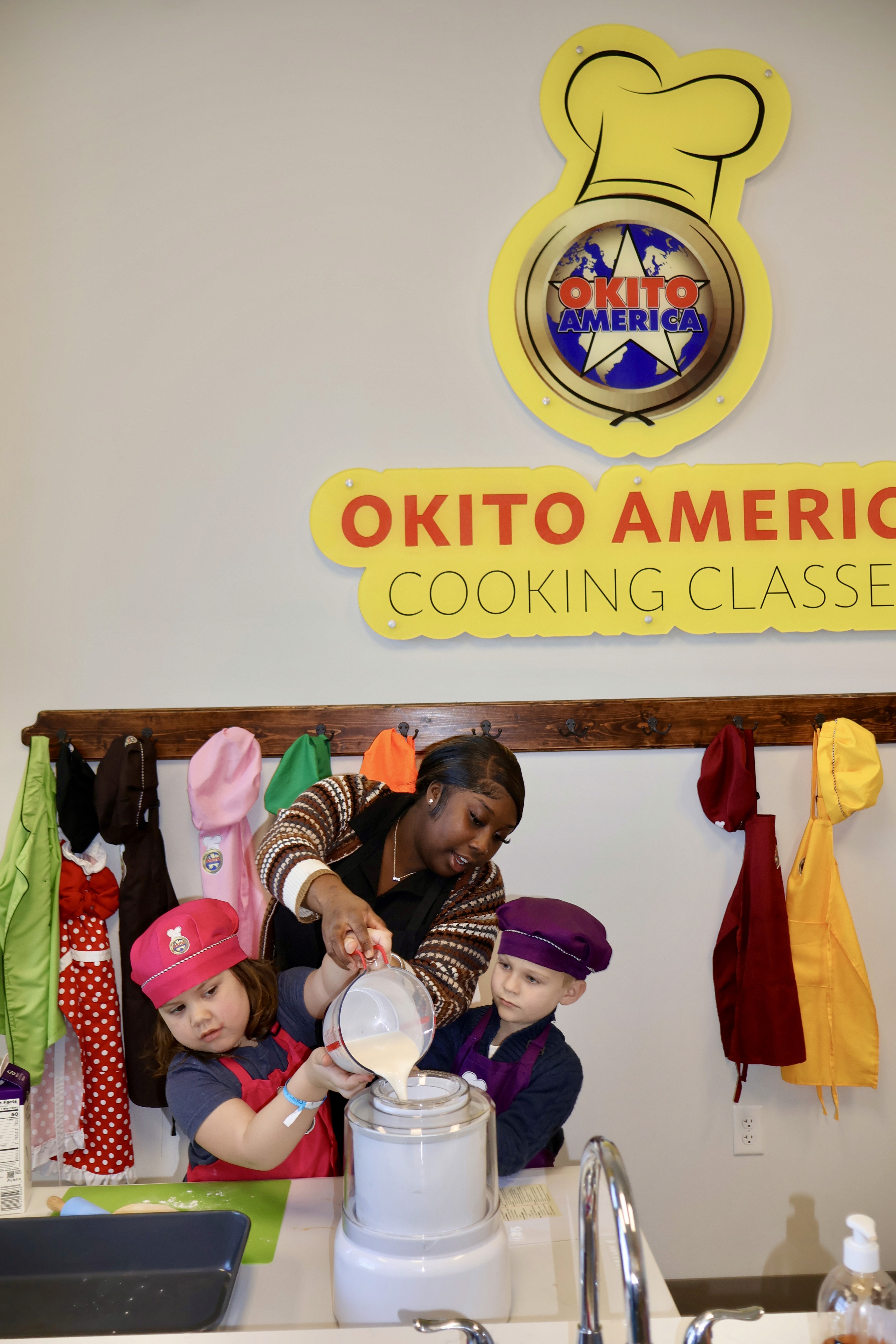 An instructor helps two young children pour ingredients into an Ice Cream mixer