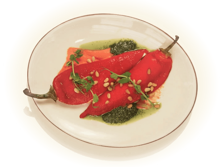 Roasted red peppers on a white plate with pesto, pine nuts, and microgreens.