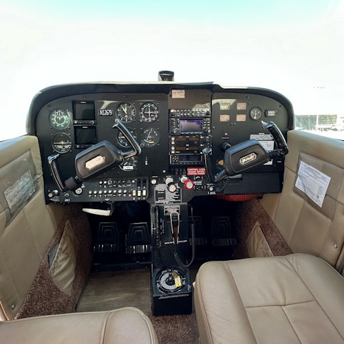 小型飞机的驾驶舱，配有双操纵杆、各种仪表盘、开关和米色座椅。
