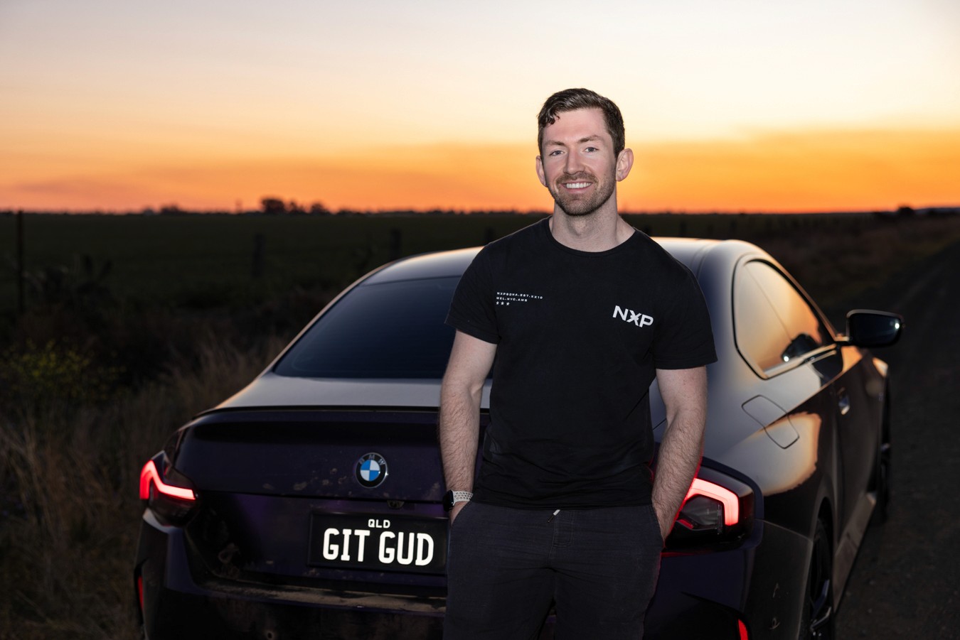 Young man standing in front of sports car at sunset