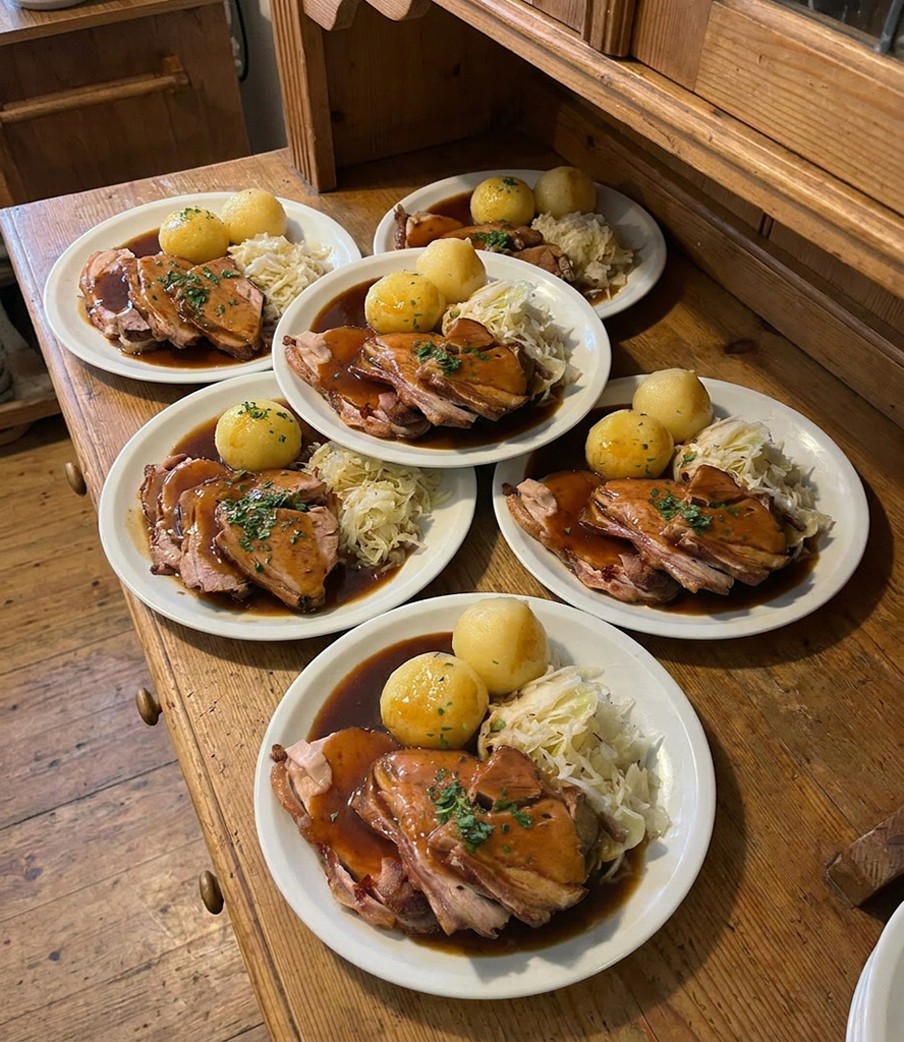 Ofenfrischer Schweinebraten Münchner Art, Dunkelbiersauce, 2 Kartoffelknödel und Krautsalat. Saftiger Braten aus der Schweineschulter schonend über Nacht gegart mit rescher Kruste