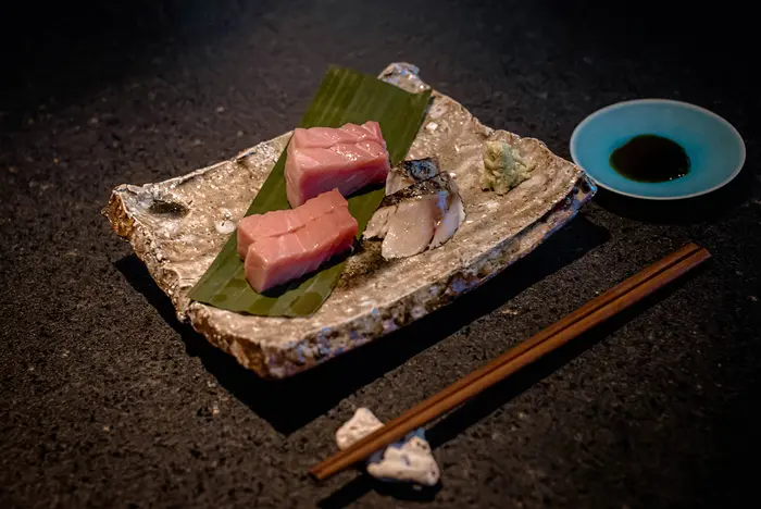 Platillo de pescado al estilo japonés servido en el restaurante japonés Kuu en Nômade Tulum, México, presentado en un lujoso plato y acompañado de palillos japoneses.