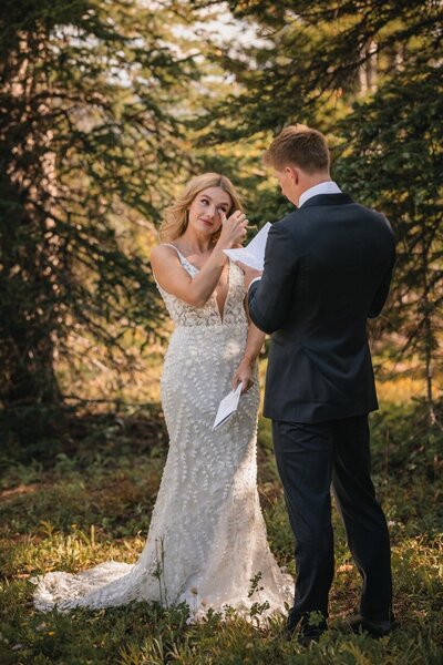 Clemmie wipes near her eye as Tucker reads from a sheet of paper in the forest.