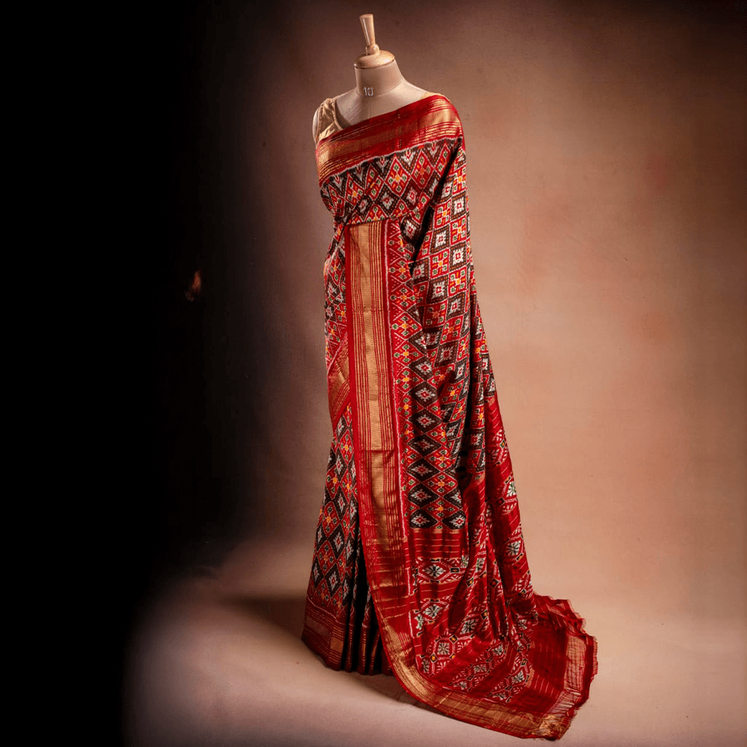 An orange Ikat saree from That Saree Shop draped on a mannequin, displaying its handwoven geometric patterns and rich traditional craftsmanship in vibrant hues.
