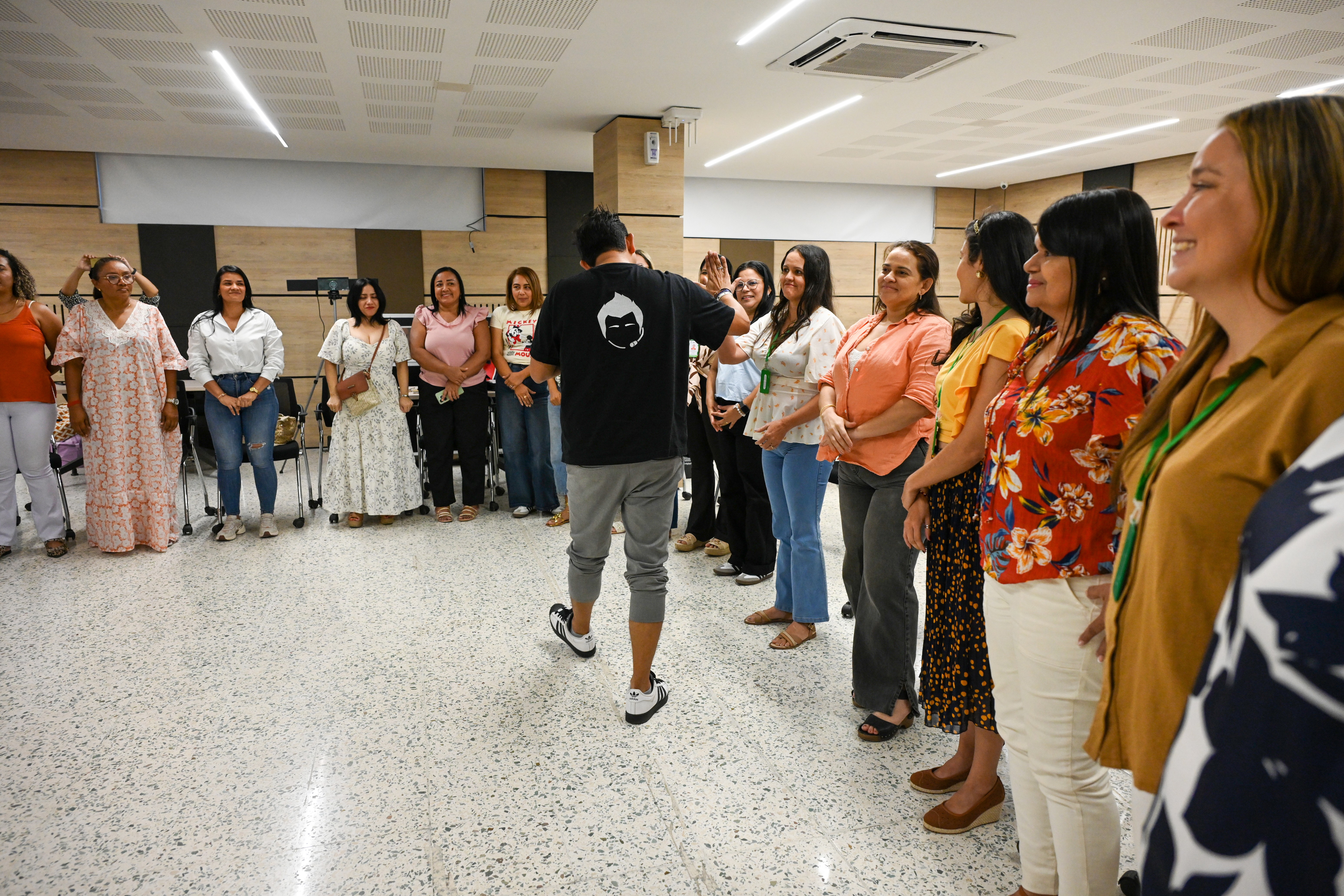 Jorge Baena de espaldas, dando una dinámica grupal con un grupo de mujeres que forman un círculo, todas sonrientes y participando activamente en una sesión de formación o taller motivacional.