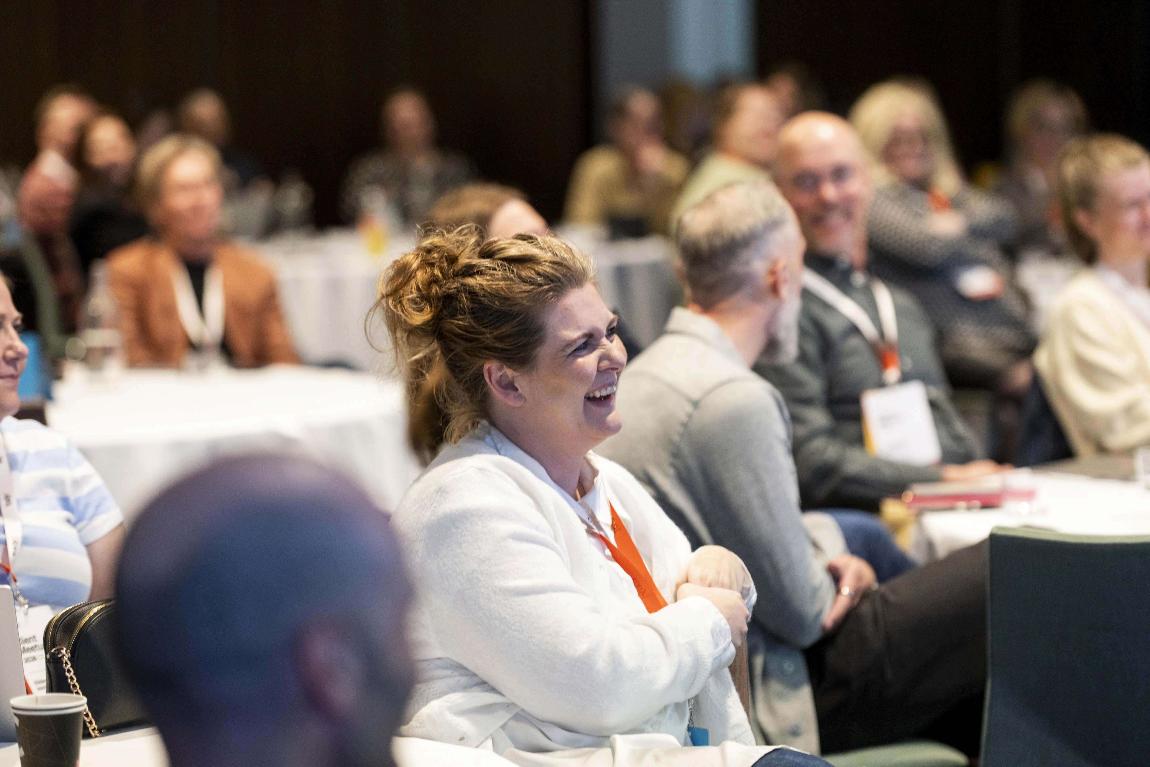 A diverse group of people attentively listening in a conference setting with some engaged and others focused.
