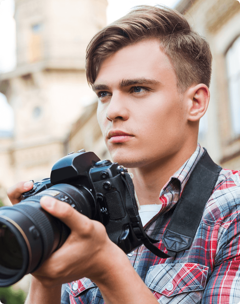 Young man with curly hair holds a vintage camera, dramatically lit in blue and red against a dark background, conveying a mysterious and artistic mood.