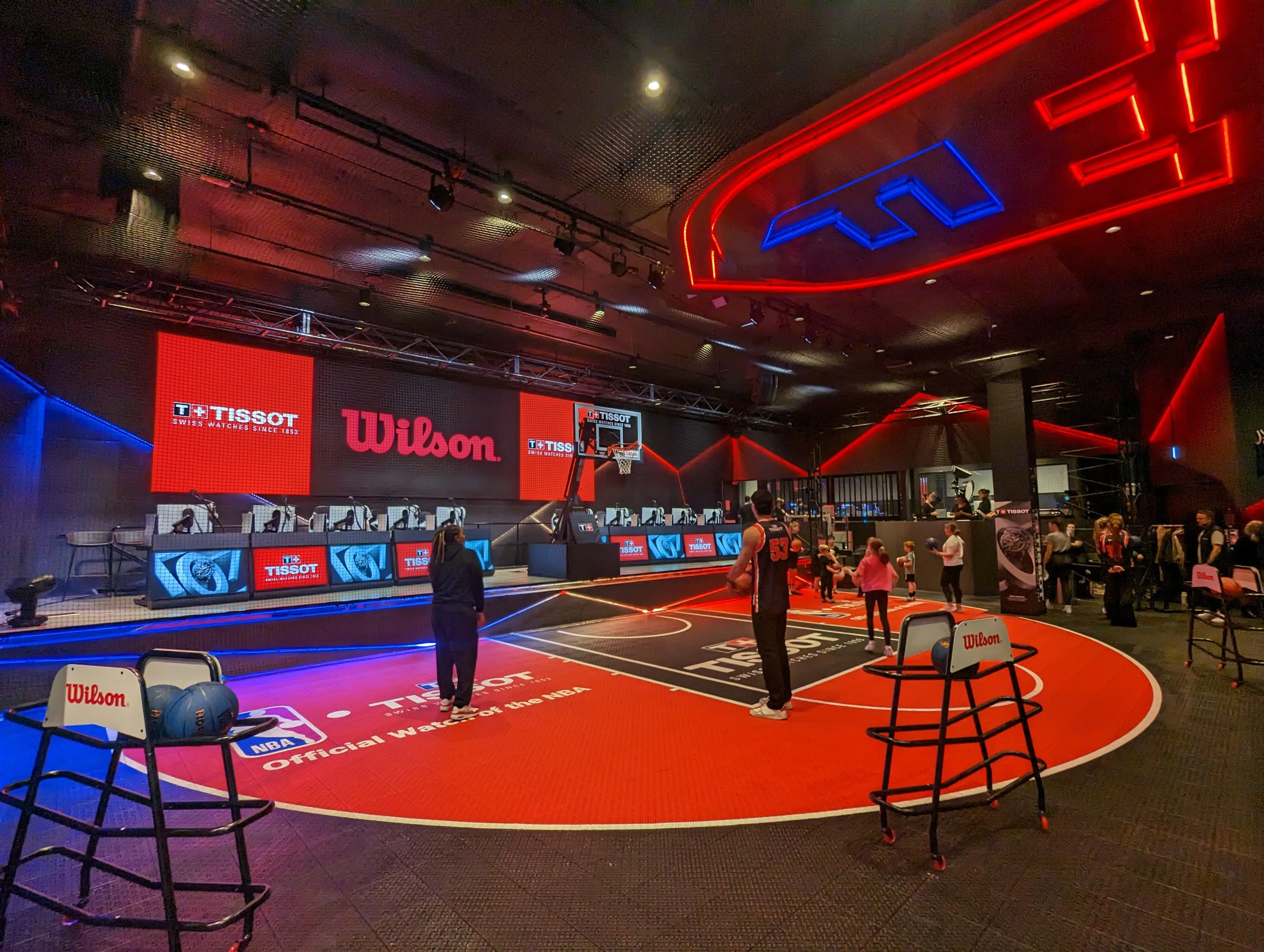 People playing on racing simulation rigs while a crowd of people watch behind in the Arena at Fortress