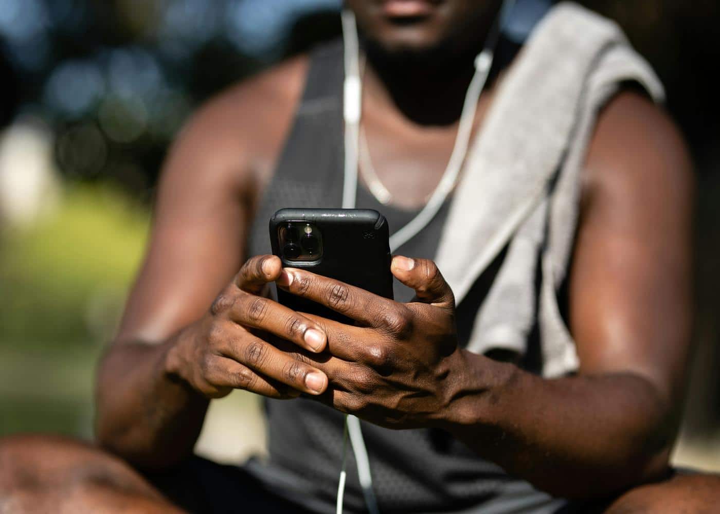 Man in workout clothes sitting outdoors looking at smartphone