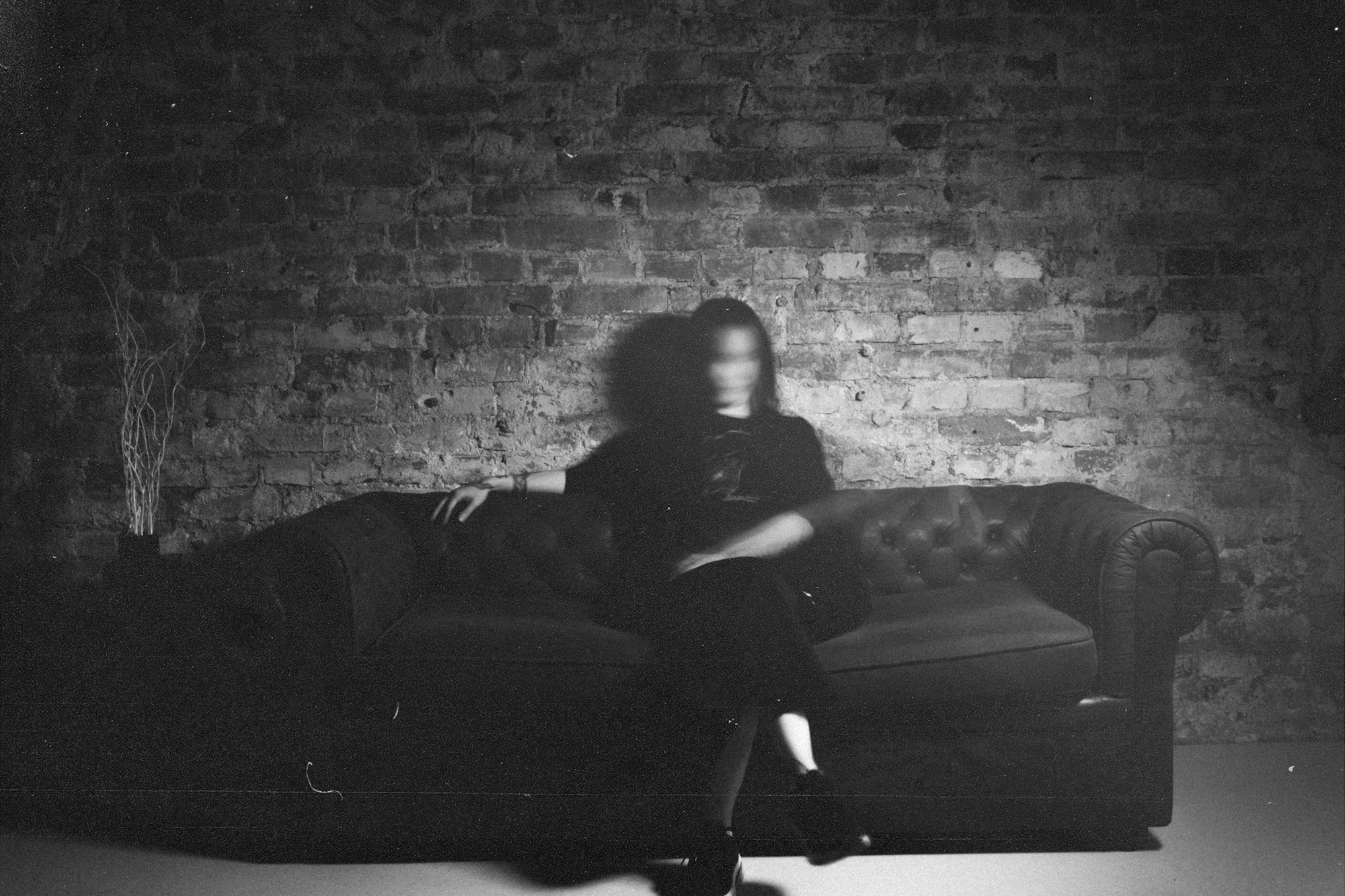 riivio sitting on a chesterfield couch in front of a brick wall, black and white, grainy
