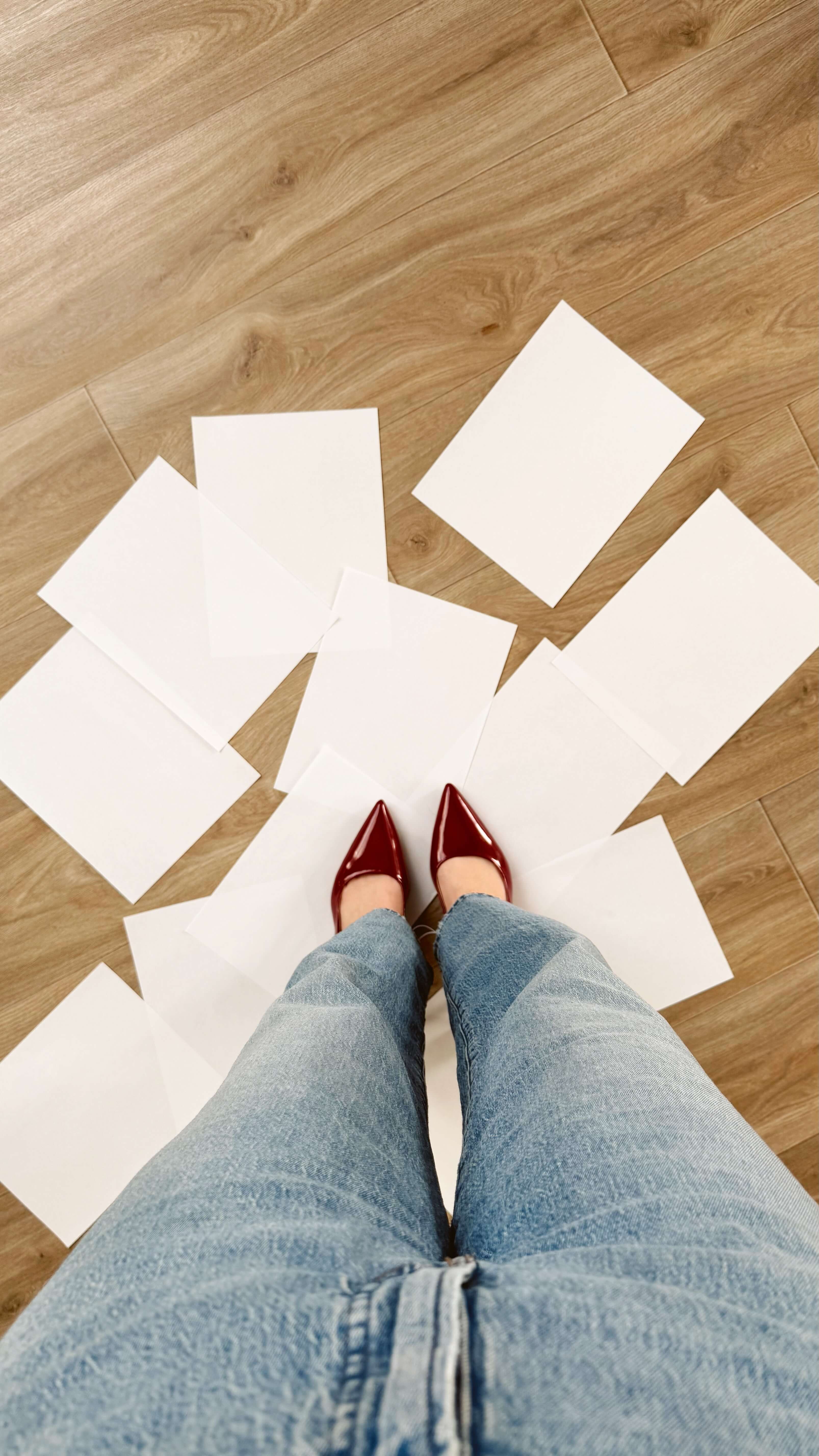 a waist down image of a woman's jeans and pointy red heels as she steps on a scattered pile of blank printer paper