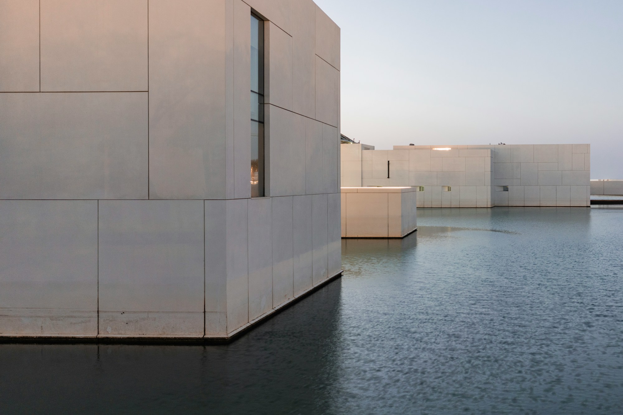 Pale lime-rendered volumes standing in still water at dusk